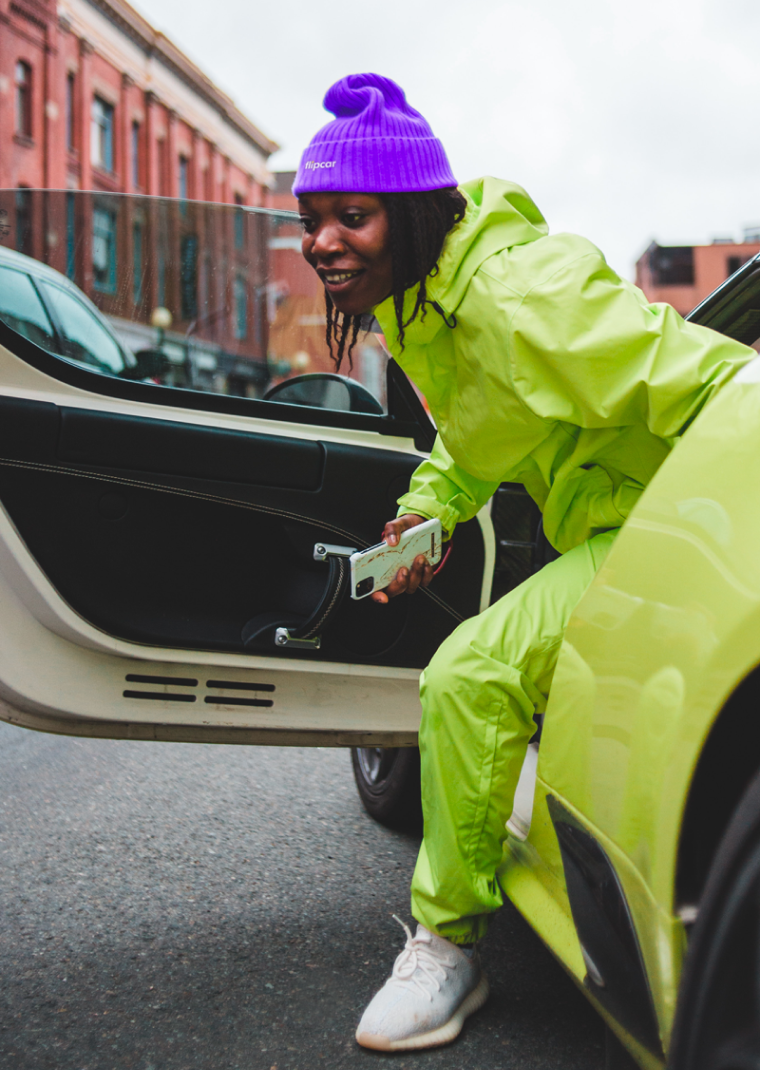 Flipcar Nutzerin steigt aus einem gelben Auto mit ihrem Smartphone in der Hand